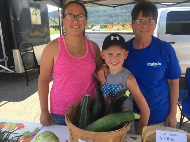 LENDING A HAND --  Eight-year-old Aiden Cooper of Wellsburg sold produce from his own garden to raise money for Follansbee flood victims. With him at the Brooke County Farmers Market are his mother Kara, left, and grandmother, Lois Wildman. 